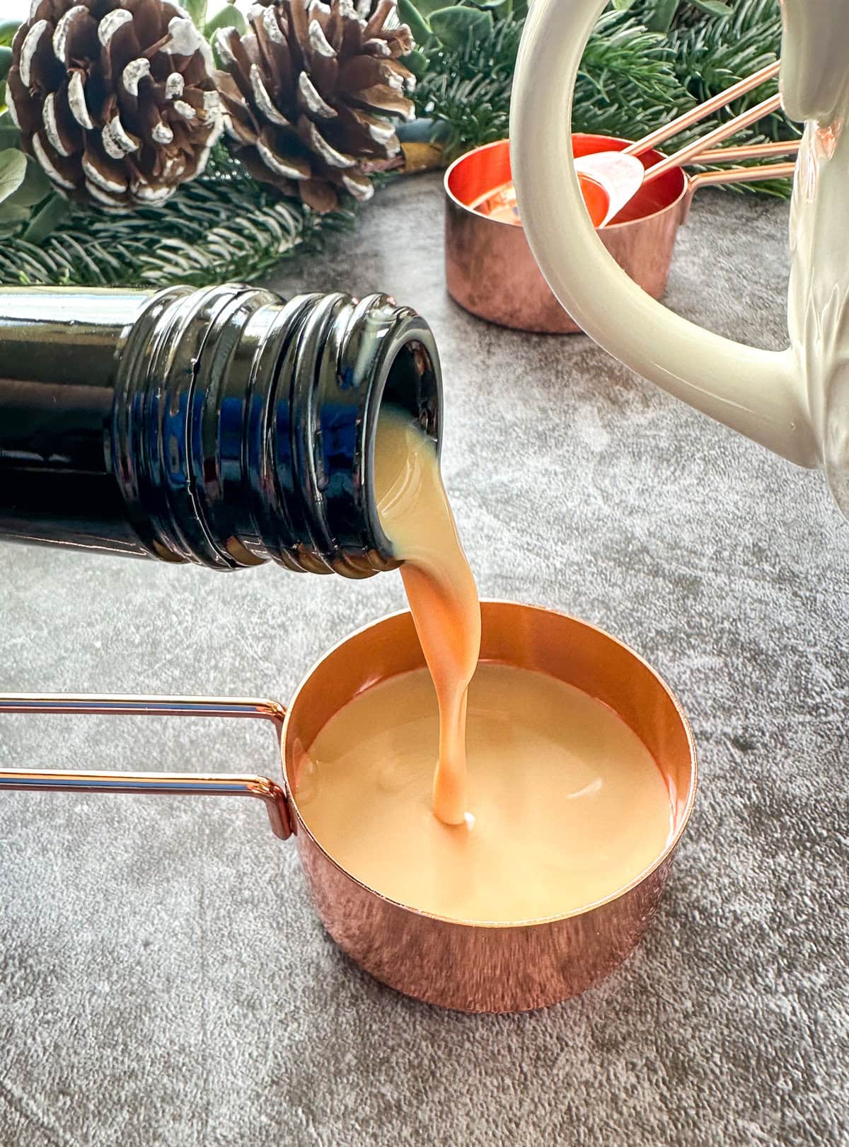 a bottle pouring Baileys into a rose gold measuring cup