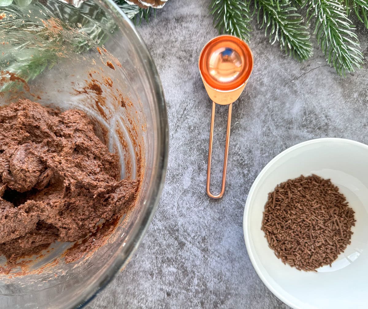 Tim Tams mixture ready to roll into balls with a small bowl of topping and a rose gold tablespoon measure