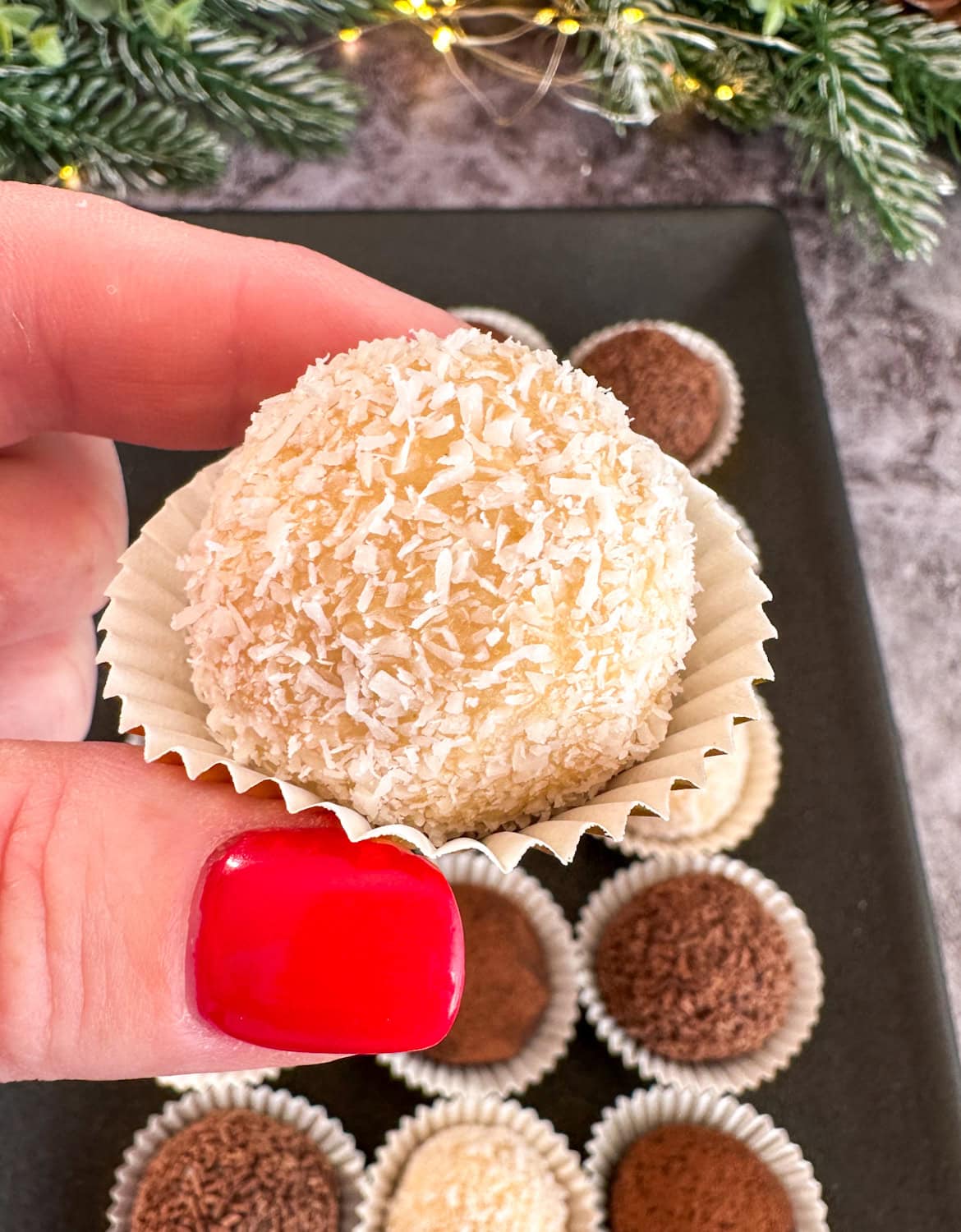 Fingers with a red painted nail holding a white chocolate Baileys Tim Tam Truffle