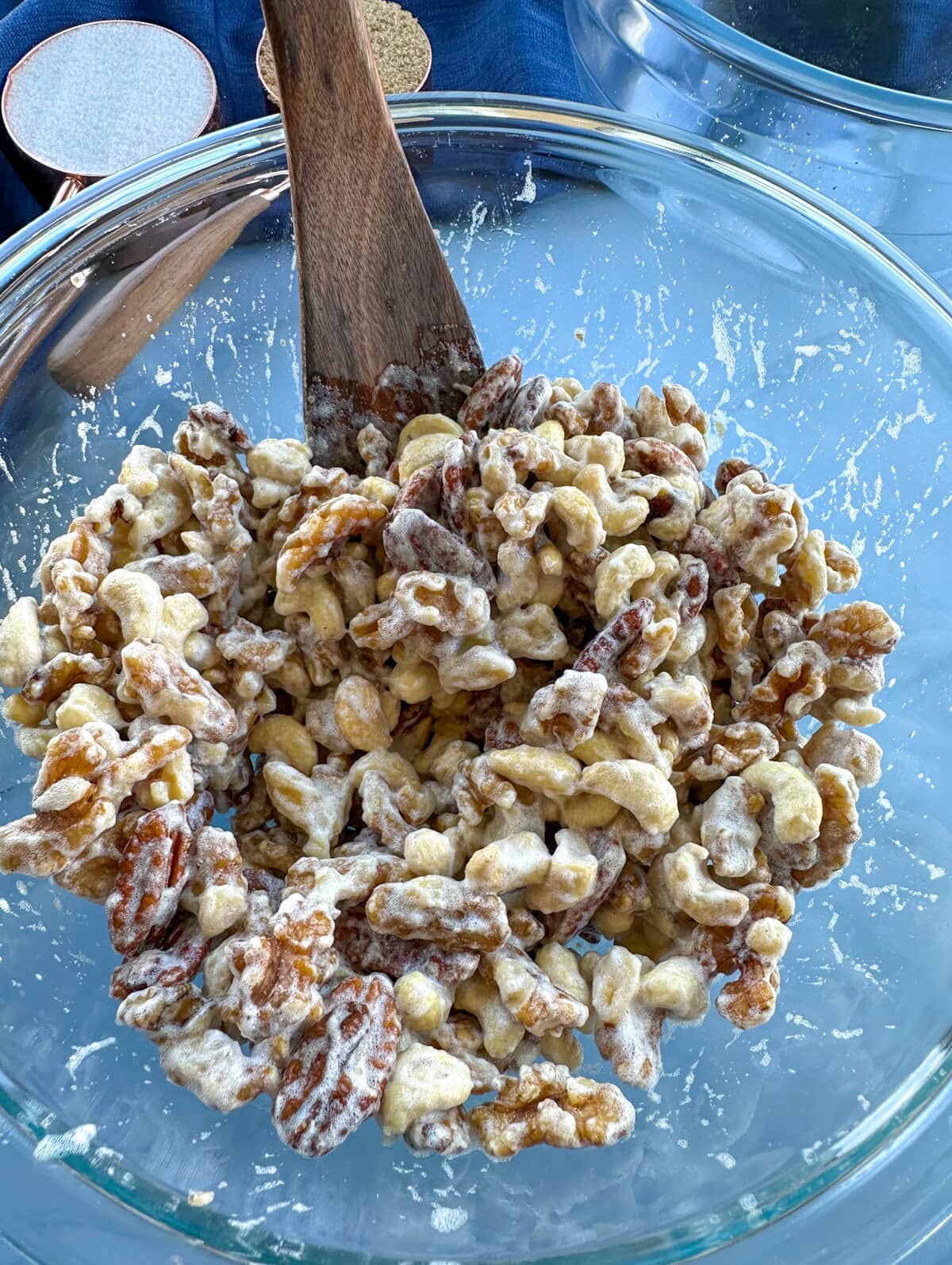 Nuts coated in whipped egg whites in a glass bowl with a wooden spatula