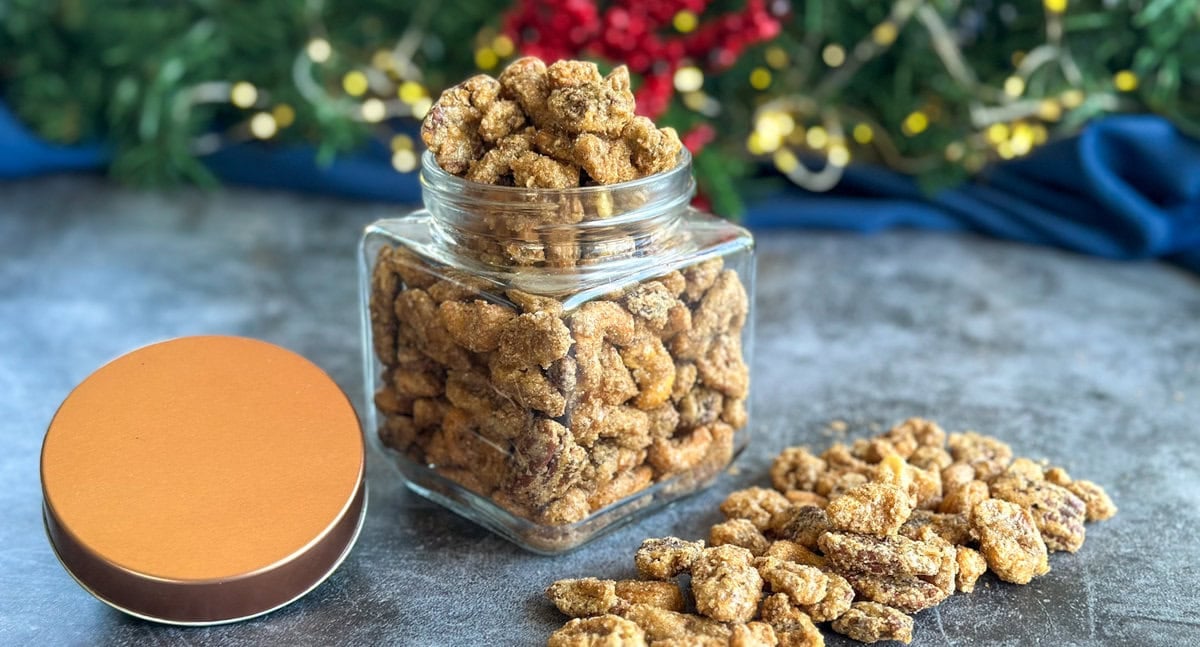 Candied Nuts in a glass jar with a rose gold lid, on a blue background with festive decor.