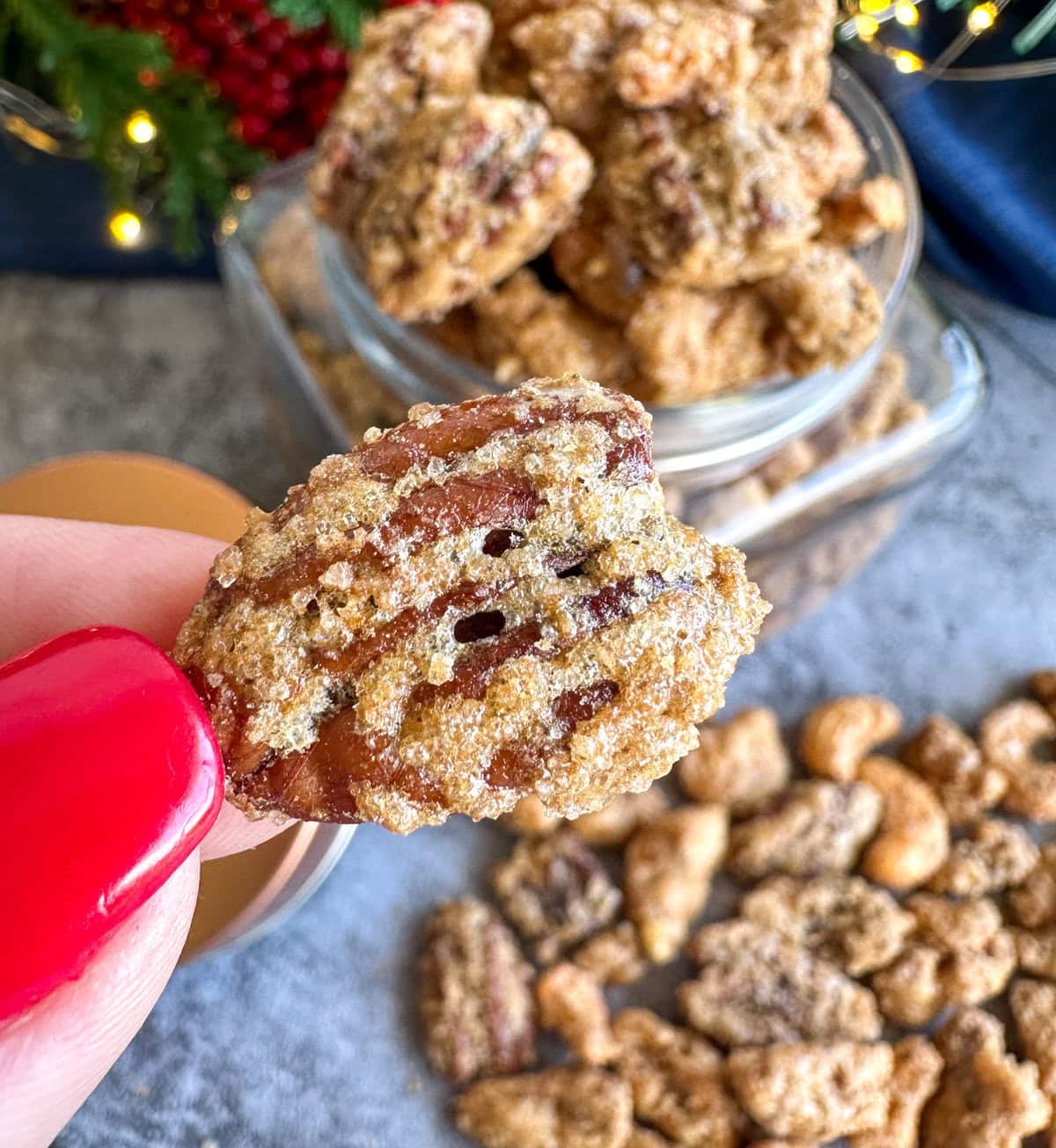 Hand holding a crunchy candied nut with red polish 