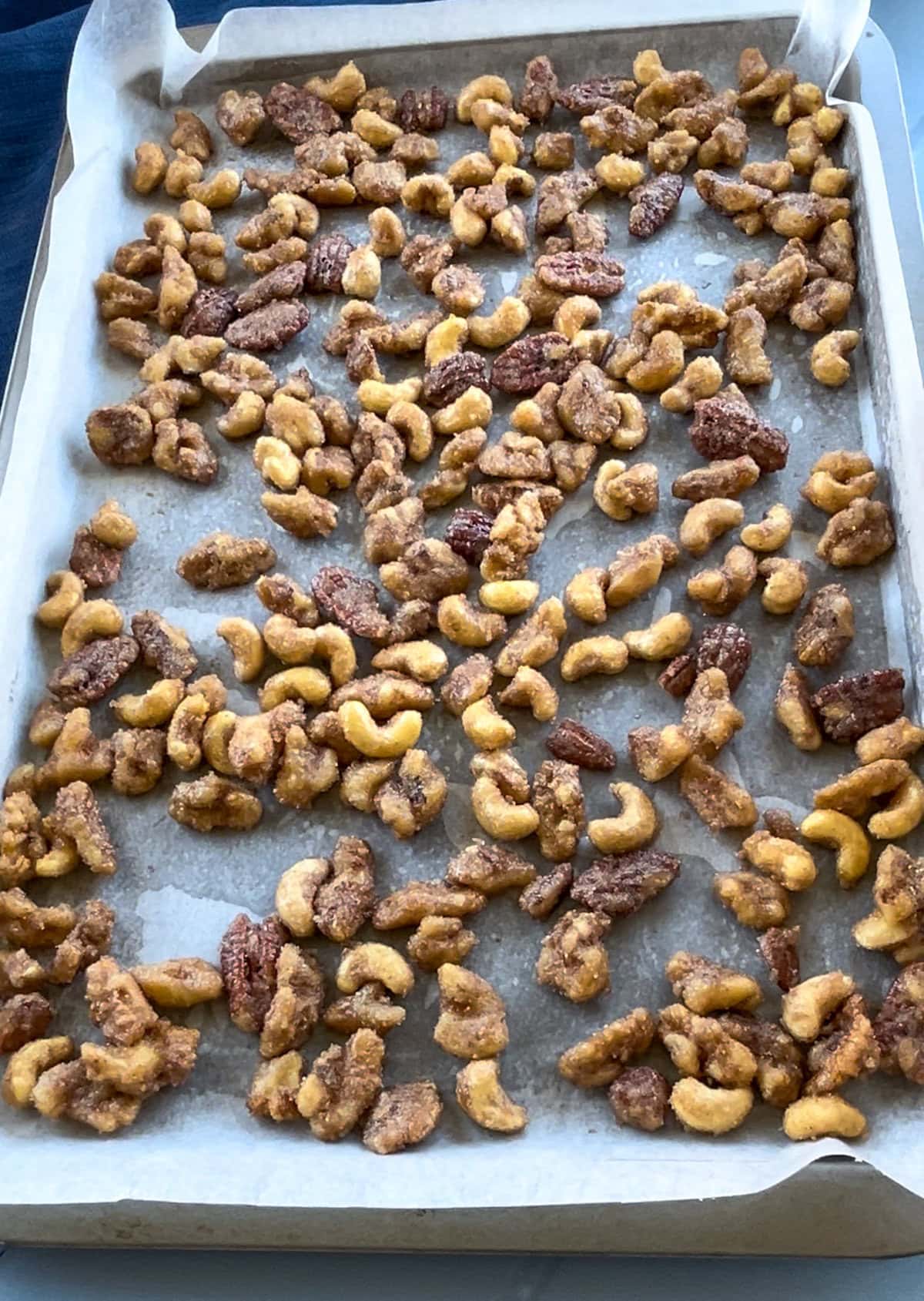 A lined oven tray with candied nuts spread evenly ready to bake