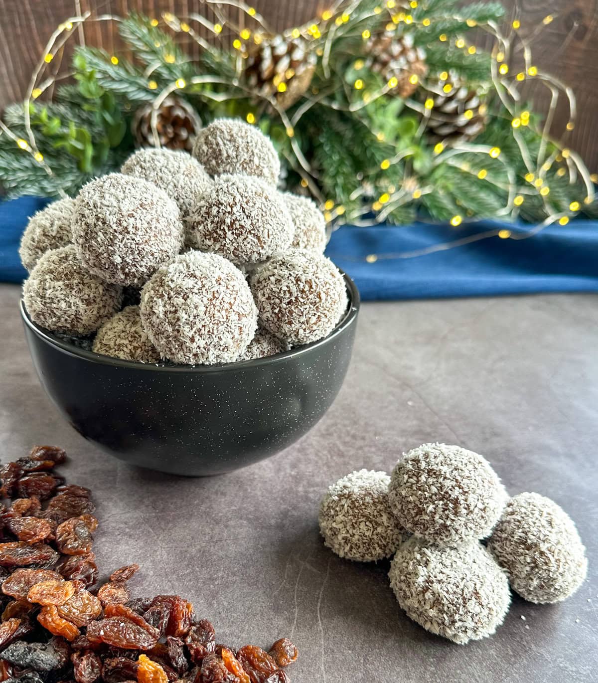 A black bowl filled with coconut coated rum and raising balls on a festive setting