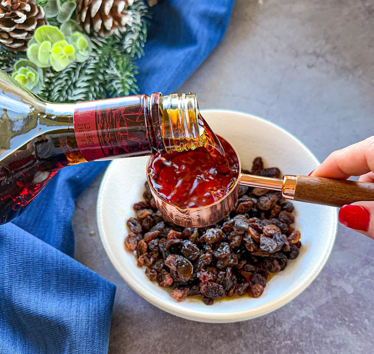 Pouring rum into a measuring cup over a bowl of raisins