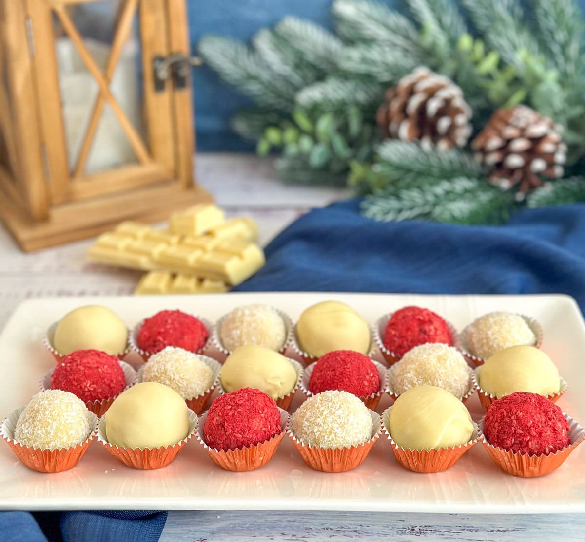 White chocolate truffles on a white platter with various coatings such as white chocolate, coconut and freeze dried raspberries on a festive table setting