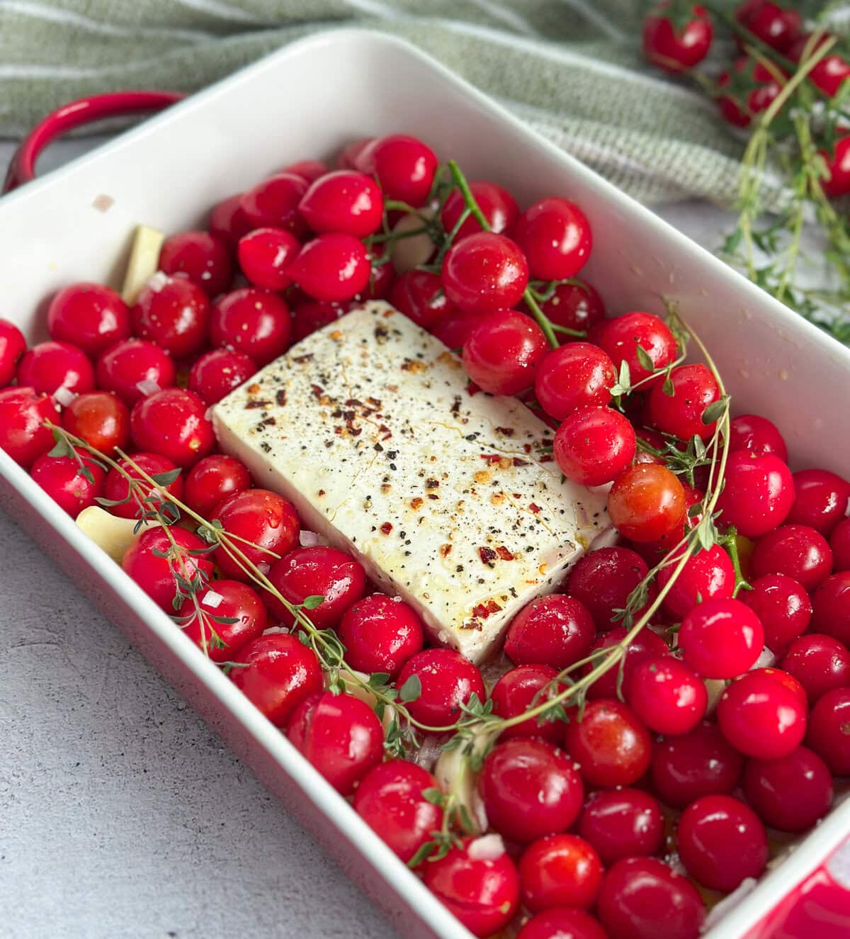 Whole rapunzel cherry tomatoes on the vine before baking with feta in a ceramic baking dish