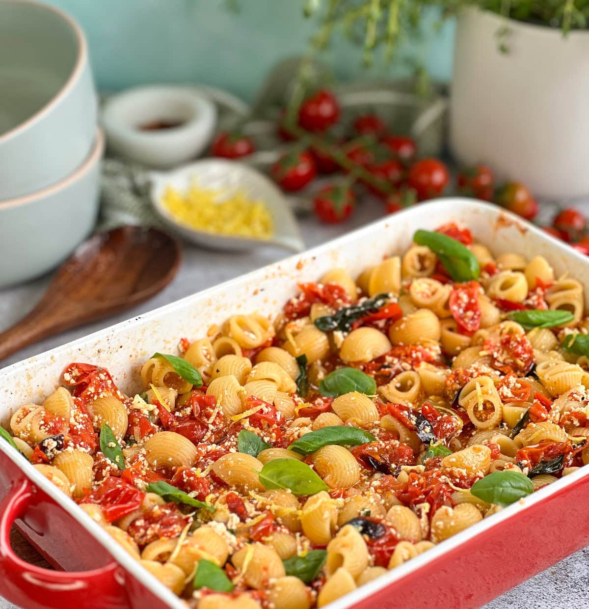 Shell pasta folded through baked feta and charred cherry tomatoes to in a red ceramic baking dish 