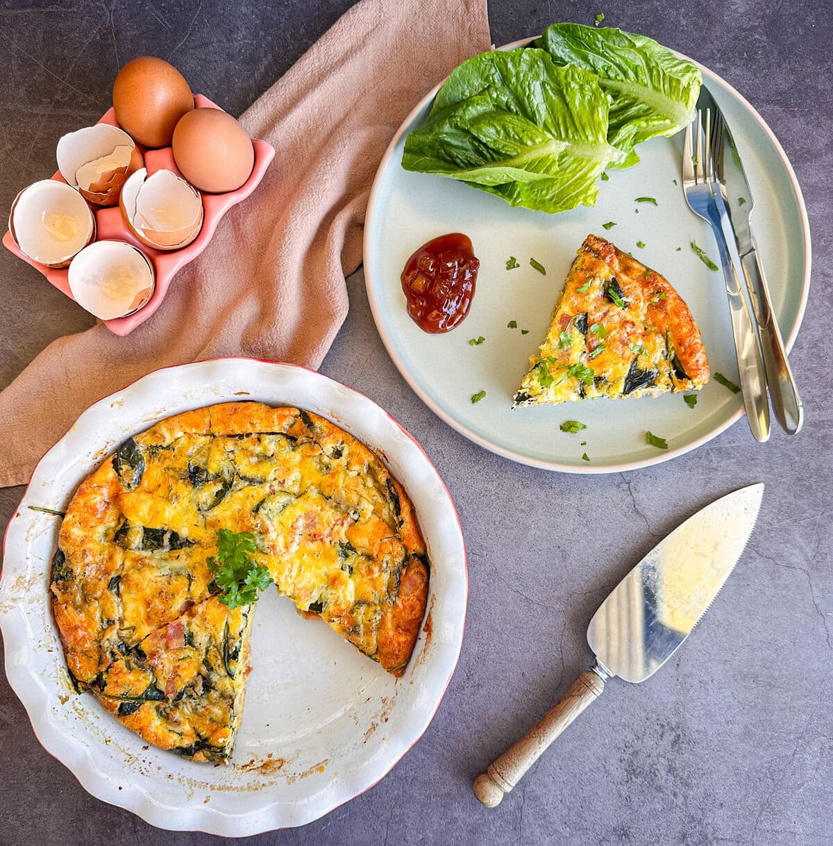 Overhead photograph of a quiche in a pie dish and a slice of quiche on a plate with chutney and lettuce. 