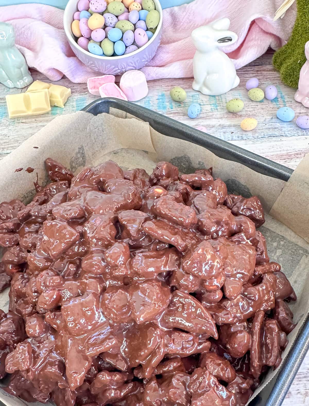 warm chocolate poured over rocky road mix placed in a slice tin before cooling