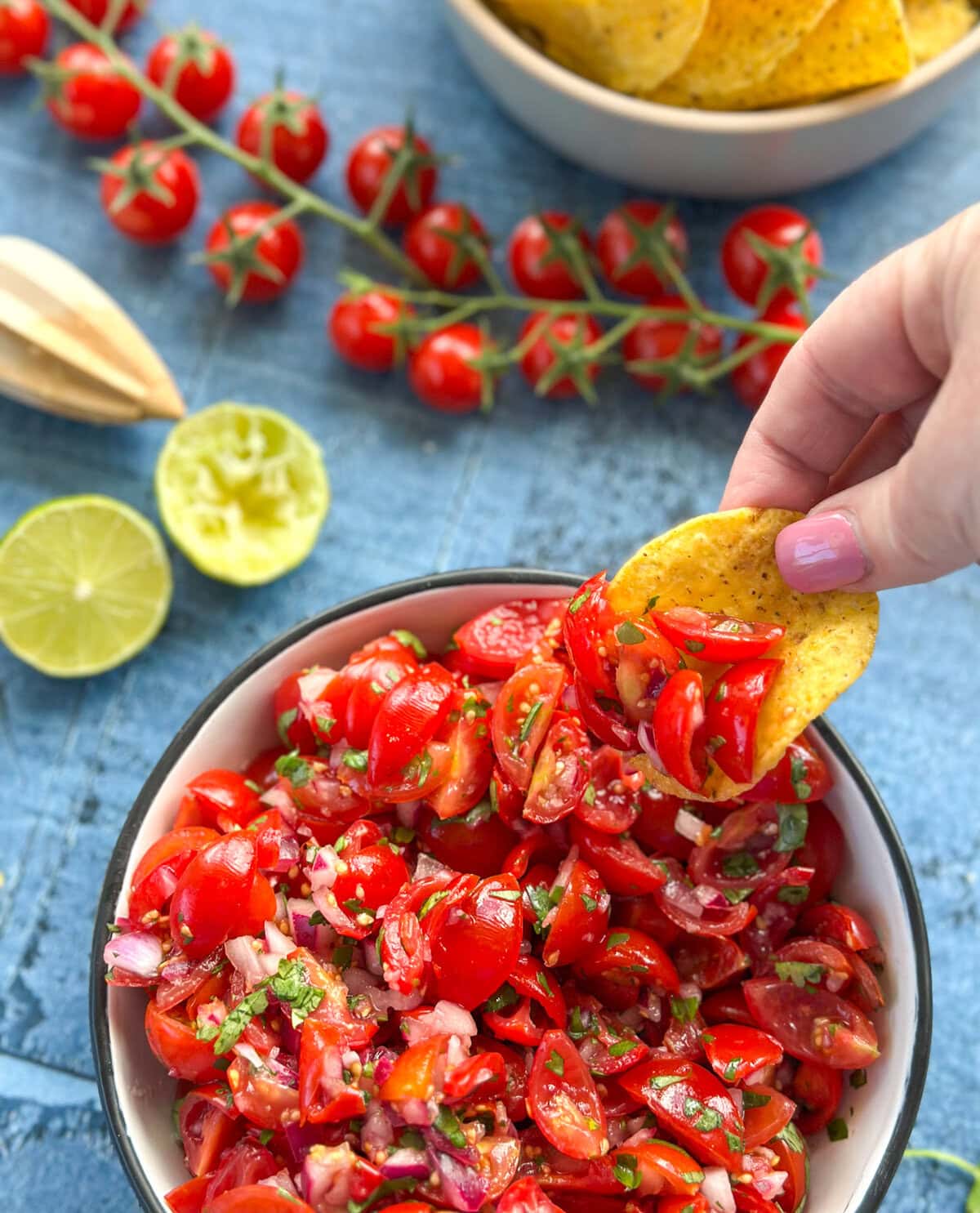 A hand with a corn chip scooping up fresh raw tomato salsa