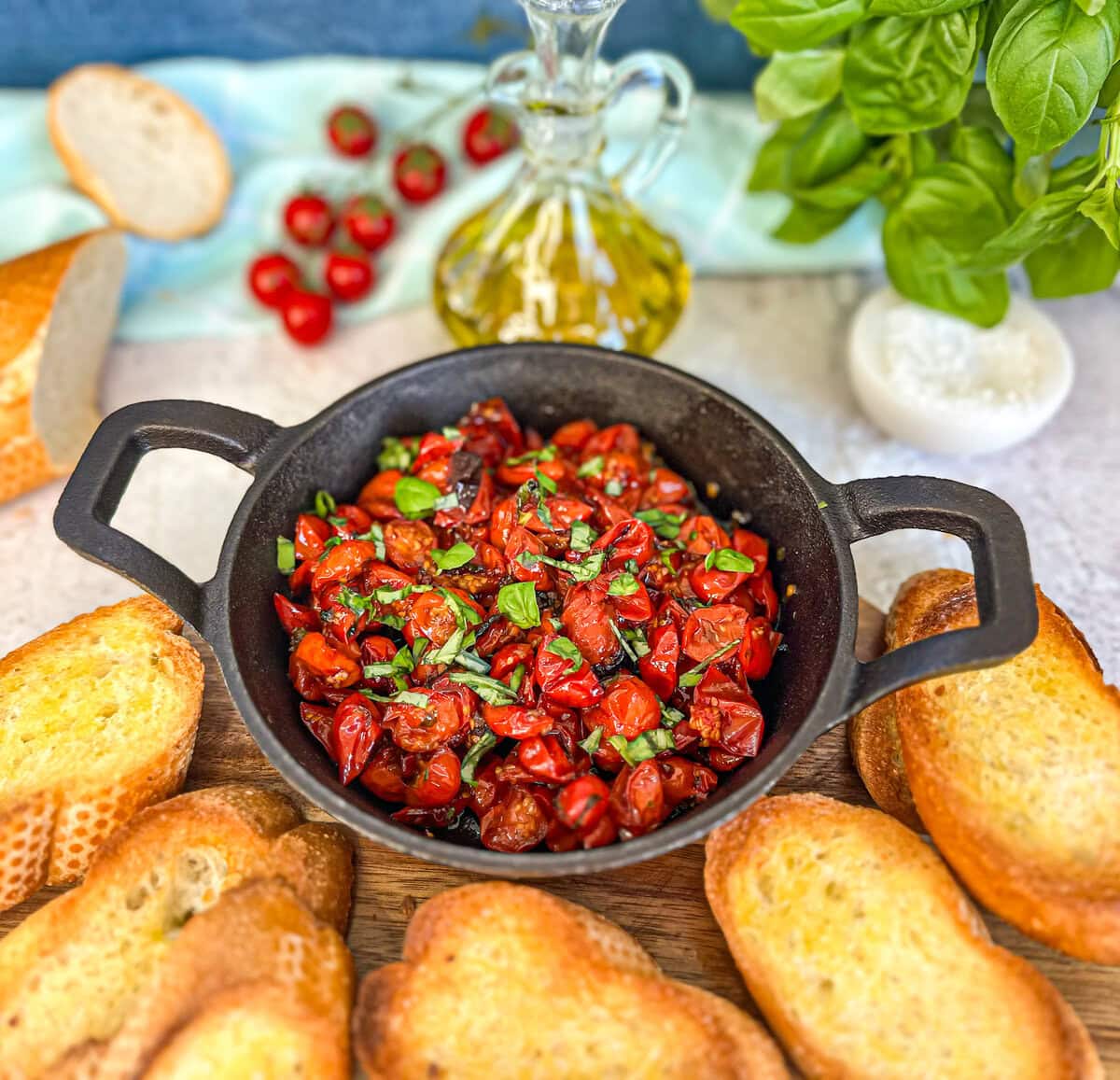 Roasted cherry tomatoes in a cast iron dish with fresh crusty golden bruschetta