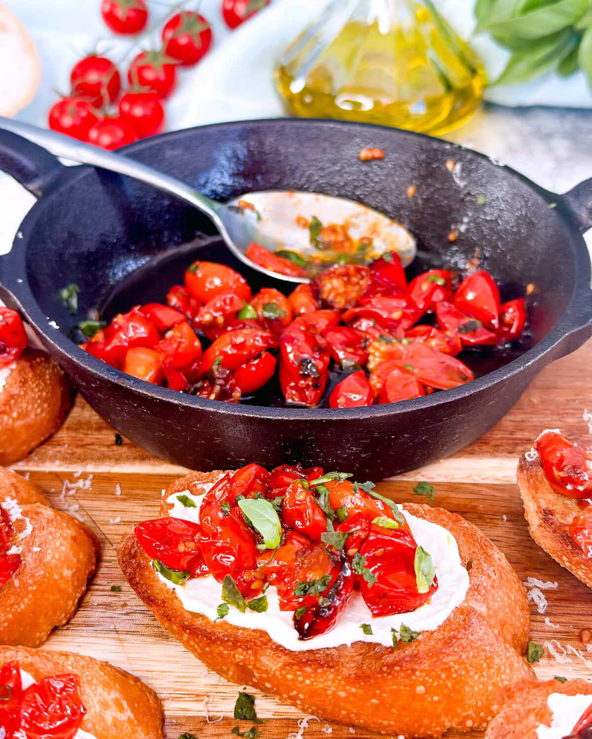 cast iron dish with charred tomatoes and crusty golden bruschetta spread with whipped feta