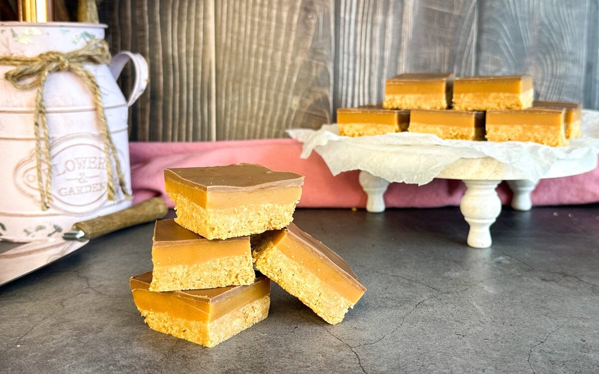 No Bake Caramel slice pieces stacked on a table and a plate on a dark background