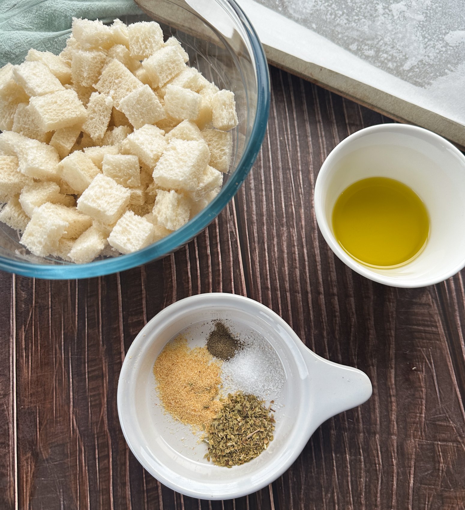 Ingredients, bowl of day old bread cubes, olive oil and salt, garlic powder and herbs for croutons