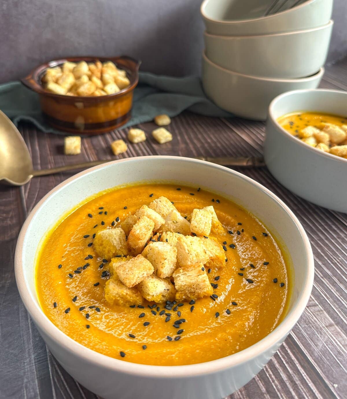 Roasted carrot and cumin soup in a bowl with croutons and black sesame seeds on a wooden table