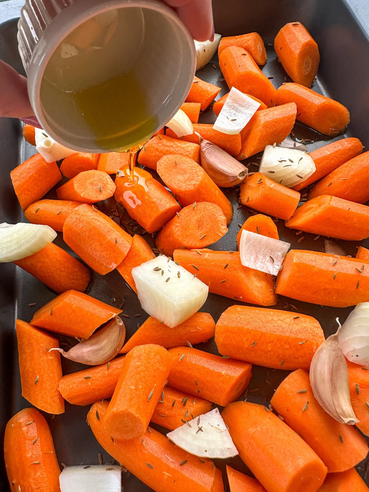 Pouring oil over vegetables before roasting for soup