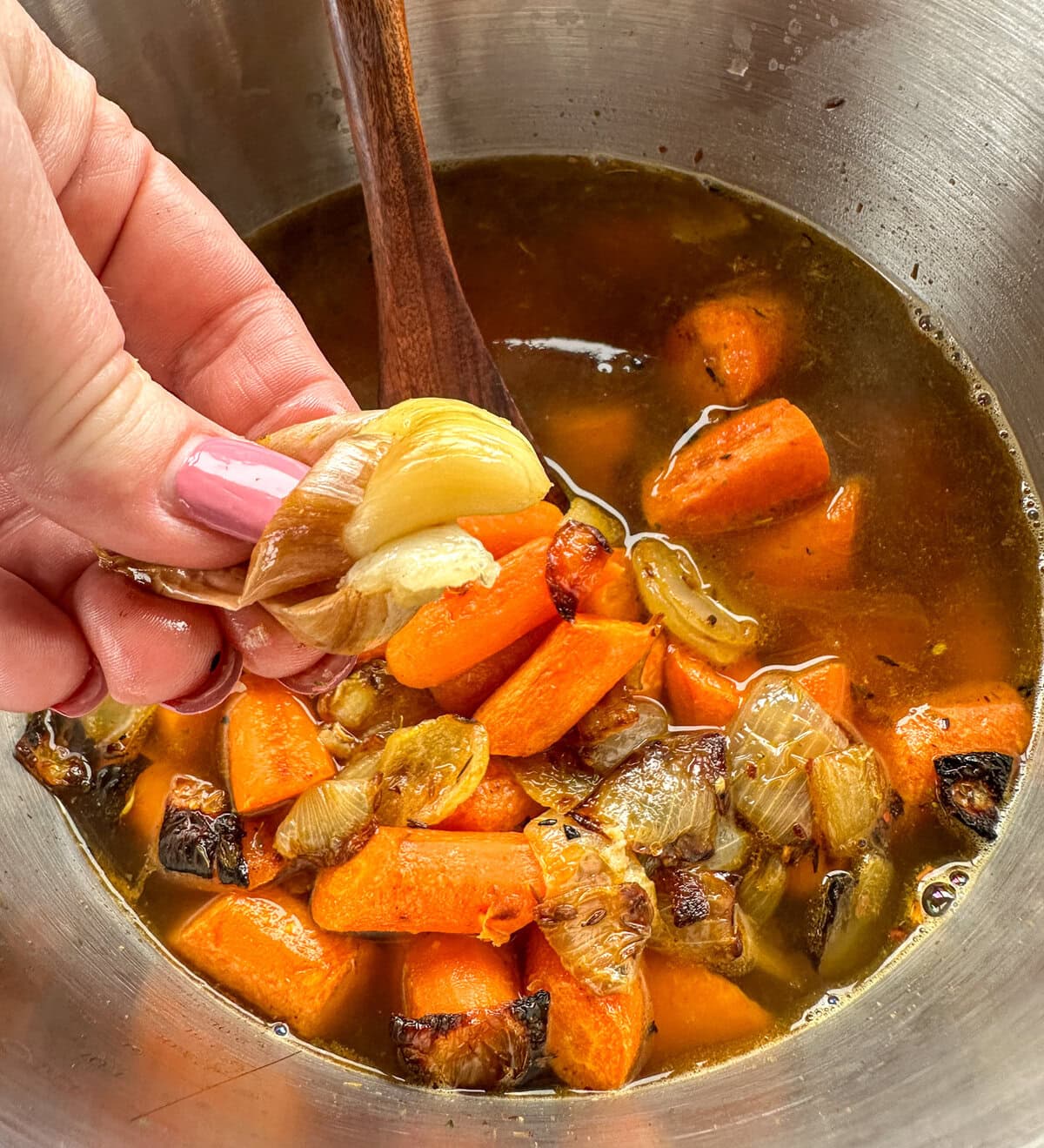 A hand squeezing roasted garlic into a soup pot.