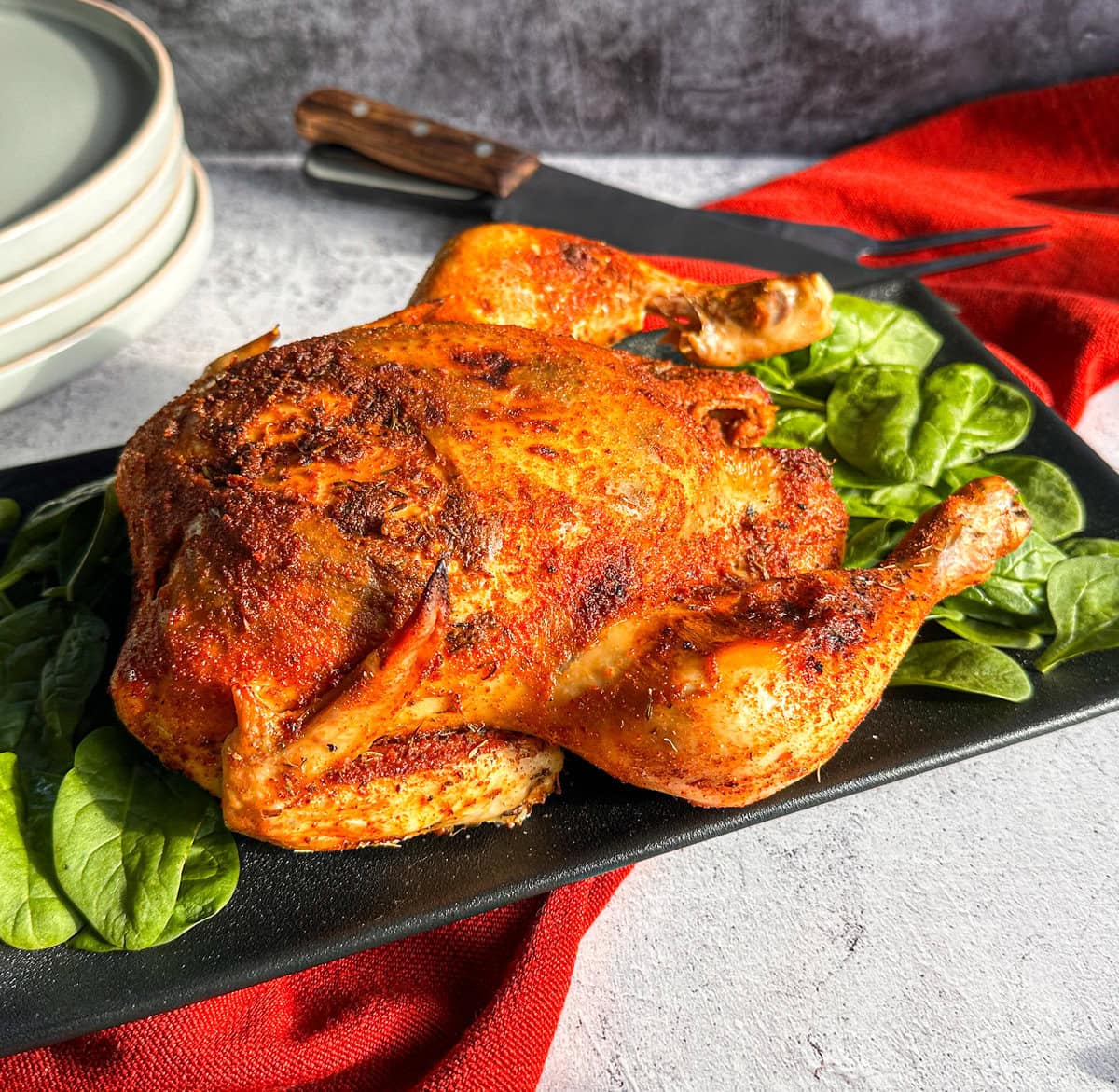 Whole slow cooked chicken on a black platter with brown crispy skin