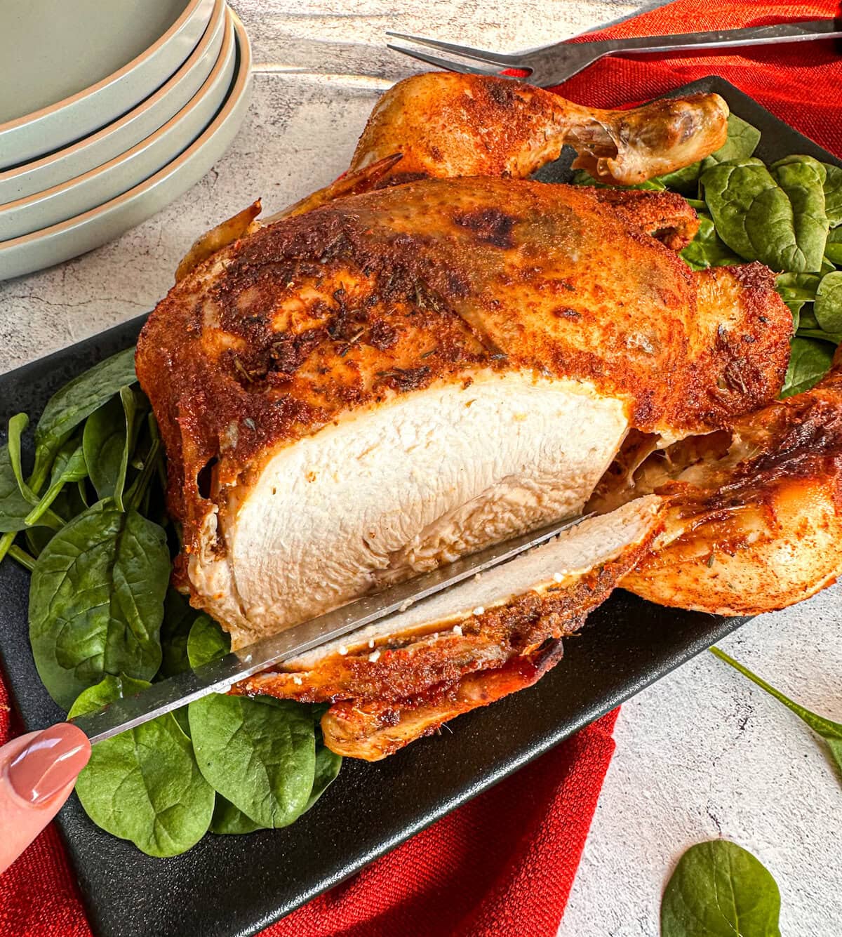 Whole slow cooked chicken with crispy brown skin, the chicken breast is being sliced open on a bed of spinach