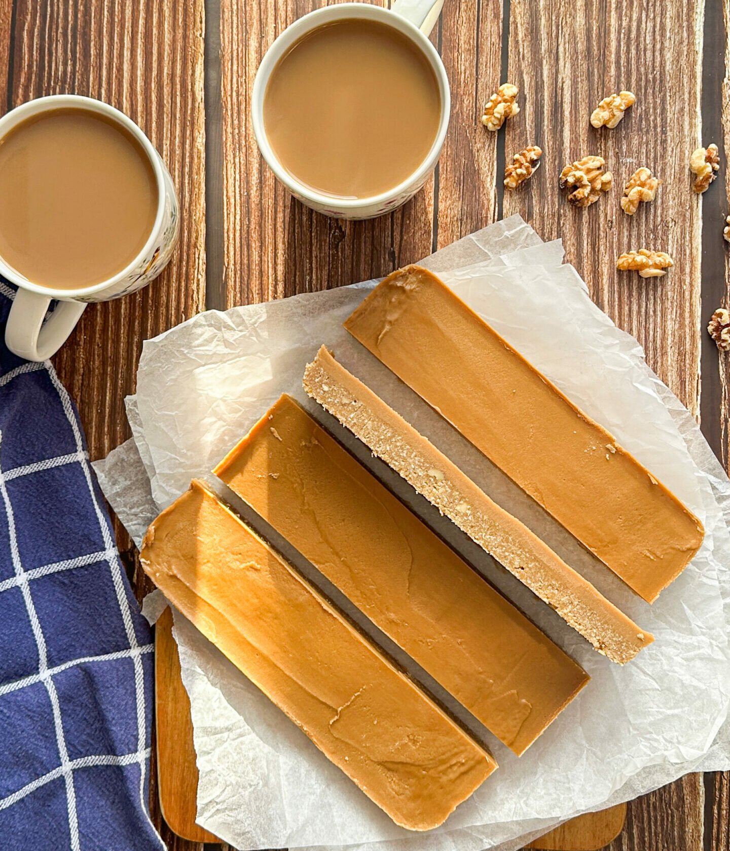 Slabs of coffee and walnut slice on a wooden table with two mugs of hot coffee in a flat lay 