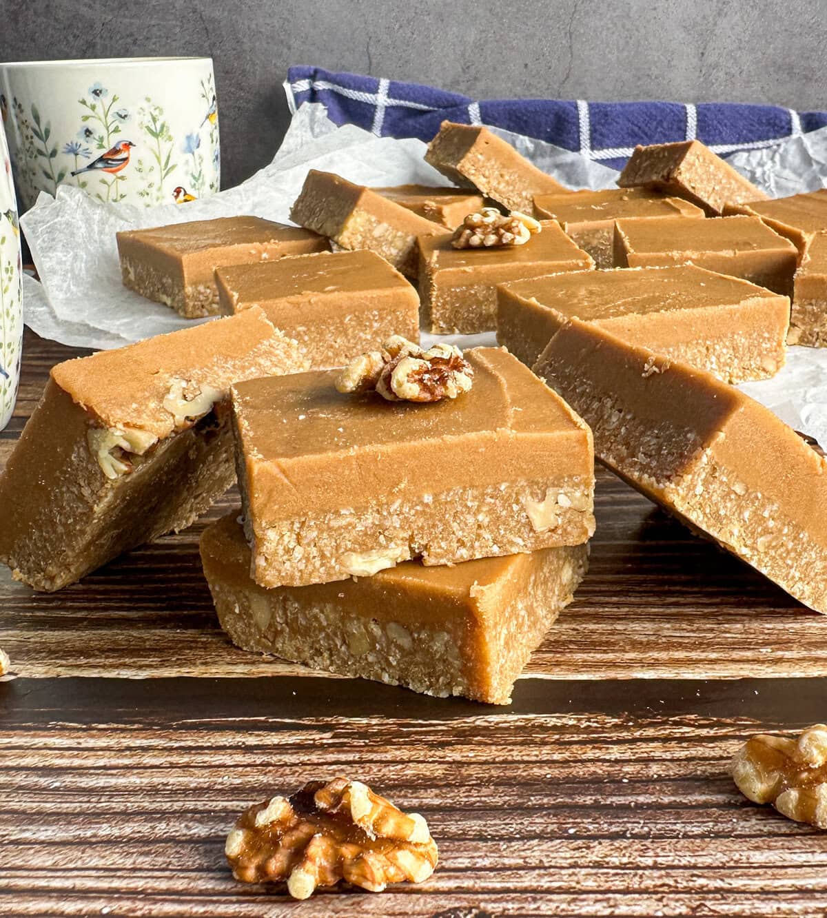 Pieces of No Bake Coffee and Walnut Fudge Slice on a wooden table with cups of coffee in the background. 