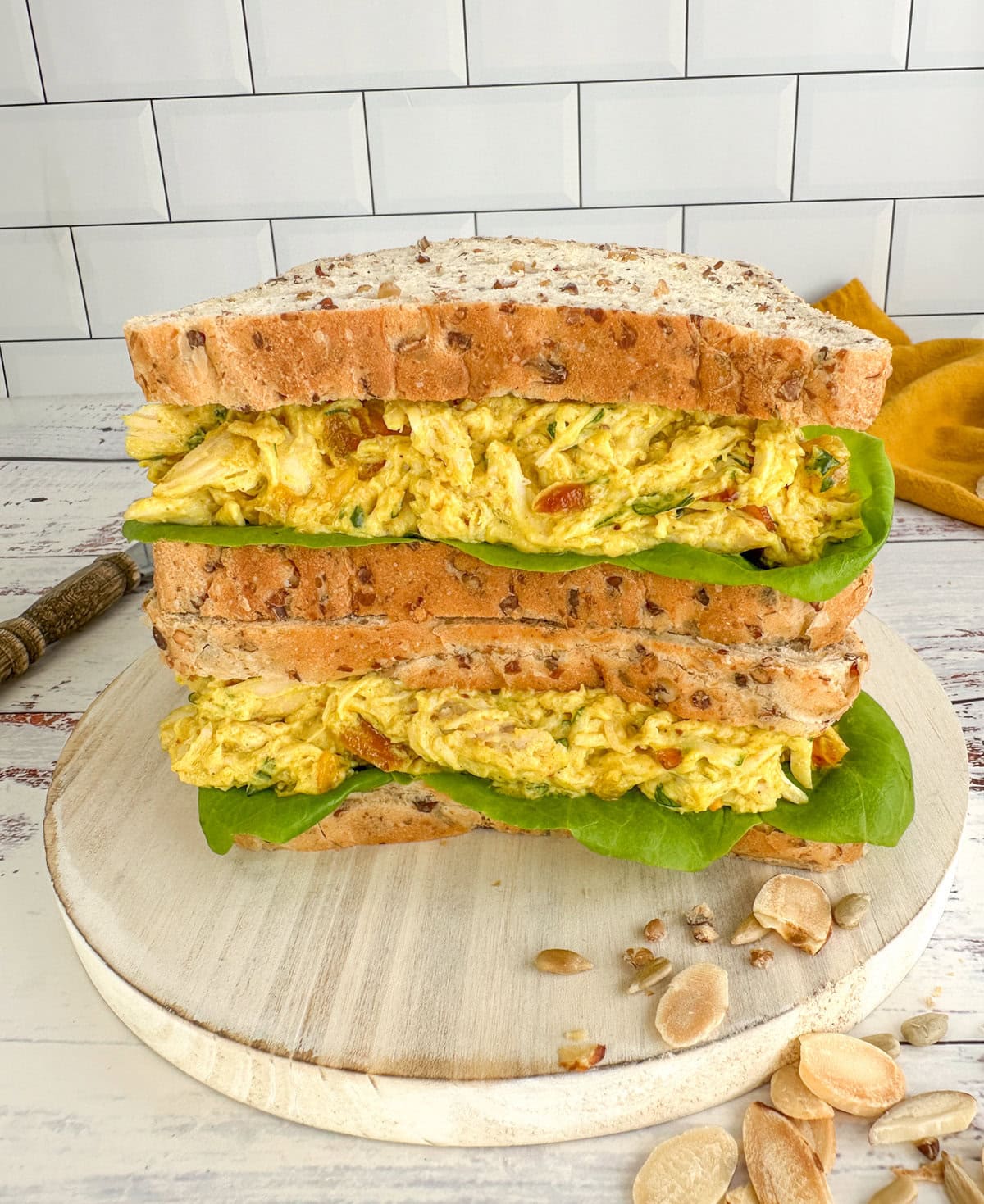 Two grain sandwiches stacked on top of each other with coronation chicken and lettuce as the filling on a white background. 