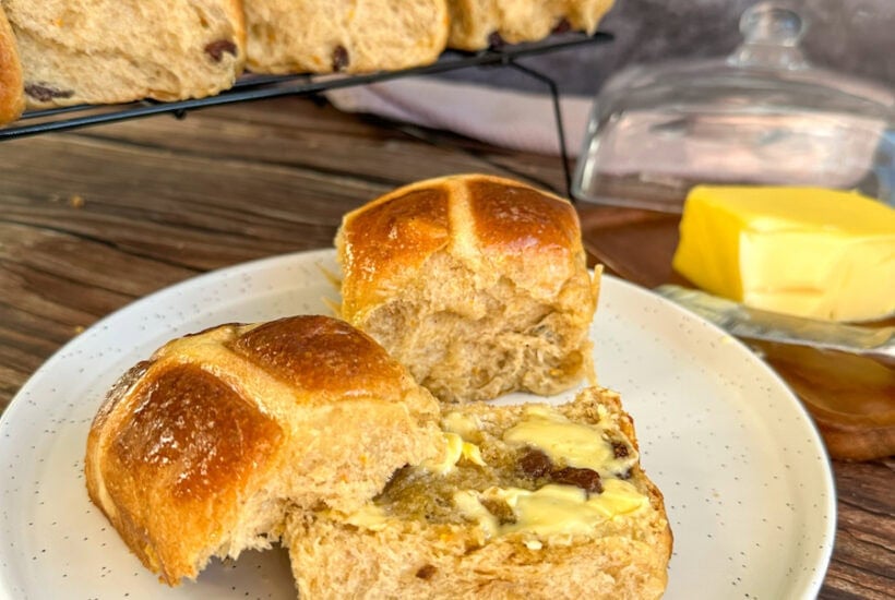 plate with a cut open hot cross bun smeared with butter